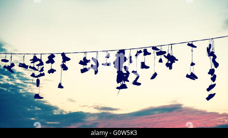 Retrò silhouette stilizzata di scarpe appeso sul cavo al tramonto, ribellione adolescenziale concetto. Foto Stock