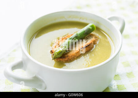 Primo piano della zuppa di asparagi in una ciotola bianca con la fetta di pane e asparagi lancia sulla parte superiore Foto Stock