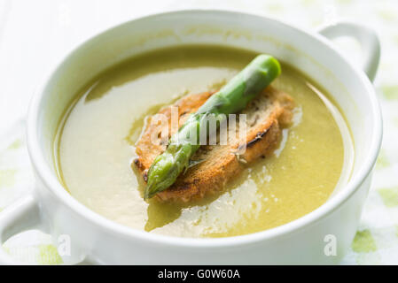 Primo piano della zuppa di asparagi in una ciotola bianca con la fetta di pane e asparagi lancia sulla parte superiore Foto Stock
