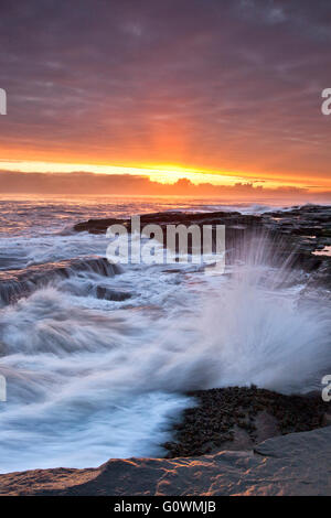 Onde che si infrangono sulle rocce al punto faro a Newbiggin dal mare sulla costa nord-orientale di sunrise. Foto Stock