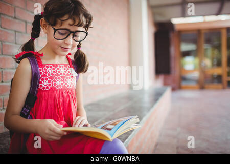 Seduto schoolgirl la lettura di un libro Foto Stock