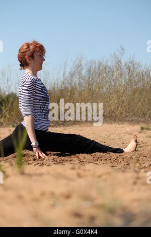 Giovane donna fare yoga asana sit in gruppi sulla soleggiata costa di sabbia Foto Stock