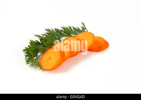 Fette e foglie di carota fresca su sfondo bianco Foto Stock