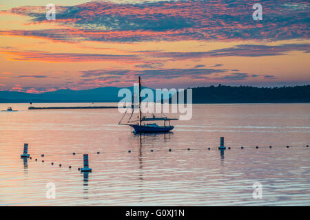 Tramonto immagine della barca a vela e il faro sul Lago Champlain con le montagne sullo sfondo preso in Burlington, Vermont. Foto Stock