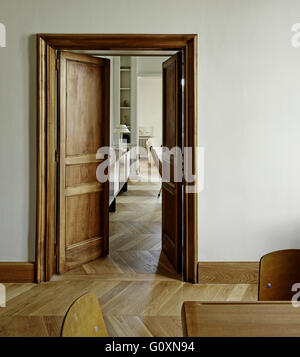 Vista parziale di un soggiorno attraverso una porta aperta, con pavimenti in parquet e un retro lato tavolo con lampada da tavolo. Foto Stock