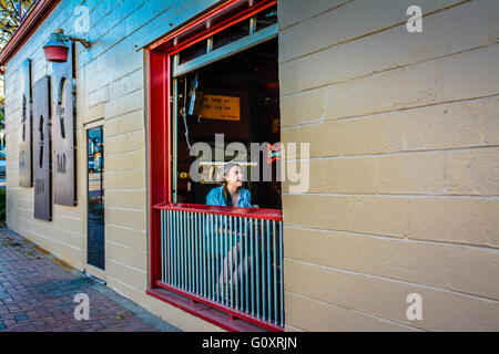 Un giovane seduto donna socializes a tavola lungo la finestra aperta al 3 Crow Bar a 5 punti nel quartiere alla moda di zona est di Nashville, TN Foto Stock