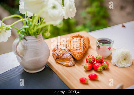 Morbido croissant francesi con bacche, una tazza di caffè e fiori freschi. Messa a fuoco selettiva. Foto Stock