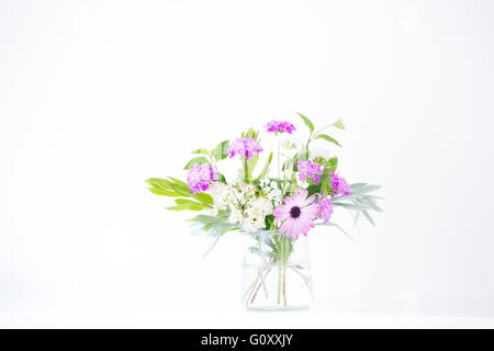 Una disposizione di fiori di primavera dal giardino, disposti in un vaso di vetro contro uno sfondo bianco. Foto Stock