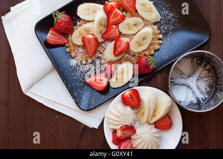 Cialde con fragole e banane sul legno rustico sfondo. Vista superiore Foto Stock