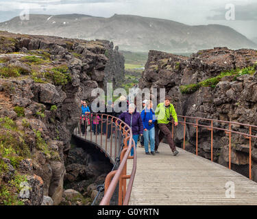 A sud-ovest dell'Islanda, dell'Islanda. Il 4° agosto 2015. I turisti a piedi su un percorso a ponte tra le pareti di roccia vulcanica attraverso il famoso canyon Almannagja a Thingvellir National Park, una Rift valley marcatura della cresta del Mid-Atlantic crinale tra il Nord America e piastre eurasiatica è una rappresentazione visiva della deriva continentale formata tra due placche tettoniche. È una delle mete turistiche più frequentate in Islanda in cui il turismo è diventato un settore in crescita dell'economia.i turisti a piedi su un percorso a ponte tra le pareti di roccia vulcanica attraverso il famoso canyon Almannagja a Thingvellir National Foto Stock