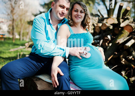 Felice famiglia incinta vestito in un turchese vestiti seduto su un moncone in posizione di parcheggio Foto Stock