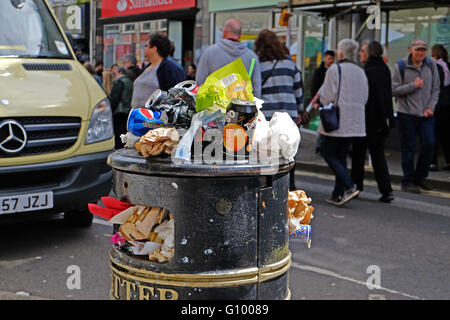 Un bidone dei rifiuti in una strada britannico traboccante di spazzatura Foto Stock
