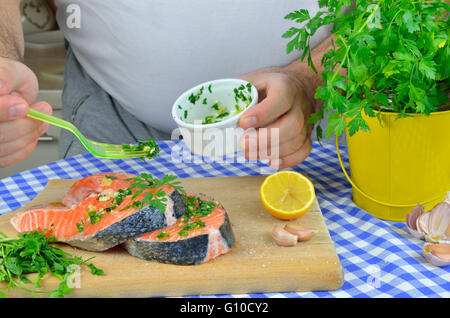 La preparazione di filetti di salmone per la cottura. Speziatura con sale, limone, prezzemolo, aglio, olio... Foto Stock