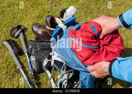 Un escursionista confezioni un rosso giacca impermeabile in una blue zaino preparando per andare a fare una passeggiata. Inghilterra, Regno Unito, Gran Bretagna Foto Stock