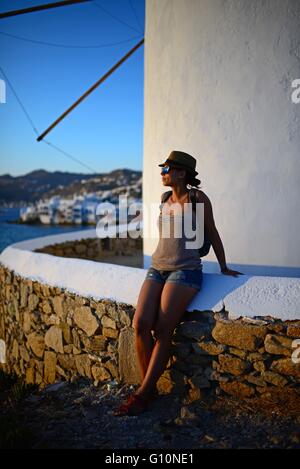 Giovane donna di godersi il tramonto da mulini a vento tradizionali (Kato Milli) a Mykonos, Grecia Foto Stock