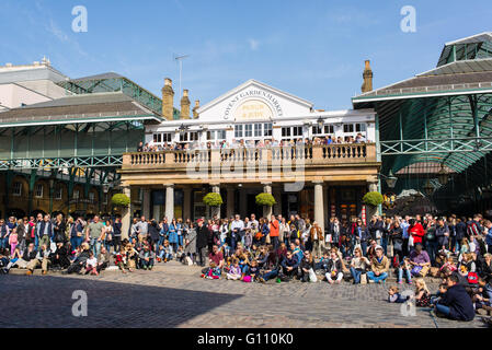 I turisti a guardare un busker mostra nella piazza del mercato di Covent Garden Foto Stock