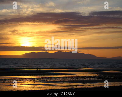 Tramonto sull'isola di Arran in Scozia, visto da Prestwick shore, Ayrshire con sabbia bagnata che riflette i colori del tramonto Foto Stock