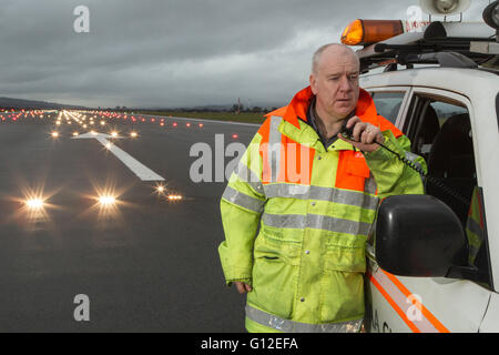 Equipaggio a terra sulla pista di aeroporto di Glasgow con luci di atterraggio in background Foto Stock