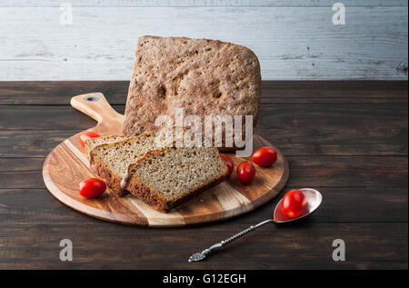 Segale scuro il pane fatto in casa con i pomodori ciliegia sulla rotonda tagliere e spazio di copia Foto Stock