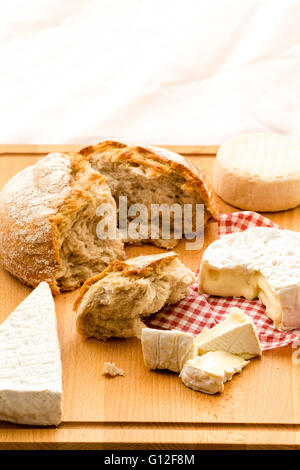 Selezione di formaggi. Round Camembert con pezzi tagliati fuori e Formaggio Brie, sul tagliere di legno con round del pane di pasta acida pane. Sfondo bianco. Foto Stock