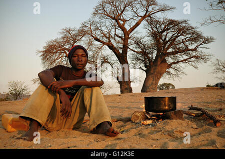 Giovane uomo per la cottura sulla spiaggia su un fuoco aperto in Chembe Village, Cape Maclear, Malawi Foto Stock