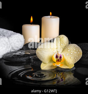 Spa sullo sfondo di orchidea gialla (phalaenopsis) su zen pietre, scende, candele e impilati asciugamani con ripple acqua di riflessione, Foto Stock