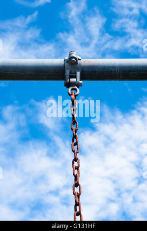 Con barra in metallo e catena arrugginita pendenti in basso dalla staffa con le viti, sul parzialmente nuvoloso cielo blu. Foto Stock