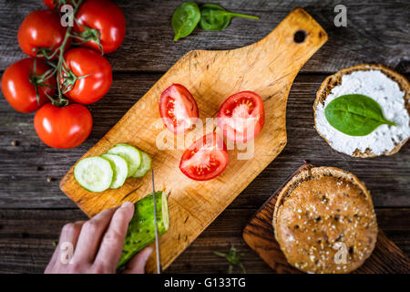 Lo Chef tagliare le verdure per insalata. Processo di taglio di vegetali per preparare un panino sano. Vista dall'alto, il fuoco selettivo Foto Stock