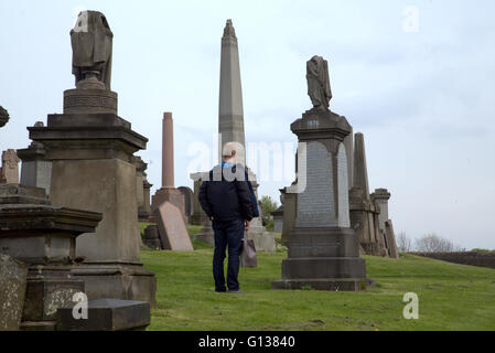 Giovane uomo sorge rispettivamente nella parte anteriore della pietra tomba nella necropoli di Glasgow, Scotland, Regno Unito Foto Stock