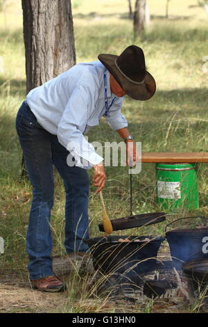 Un paese più maturo lady cottura con forni di camp o olandese forni, in un campo di fuoco per la carità Eidsvold Cattle Drive in QLD. Foto Stock