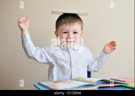 Giovani schoolboy giocando con libri e sorridente come egli siede alla sua scrivania in aula Foto Stock