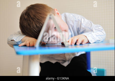 Giovani schoolboy giocando con libri e sorridente come egli siede alla sua scrivania in aula Foto Stock