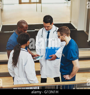 Gruppo multirazziale di medici in una riunione improvvisata in piedi su una rampa di scale in cerca di informazioni su un computer tablet, visualizzare f Foto Stock