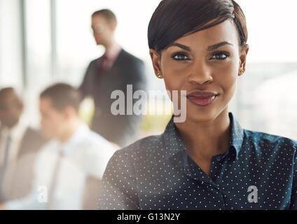 Vicino sul sorridente bella donna d'affari con luce flare sulla spalla dalla grande finestra in ufficio con il gruppo Foto Stock