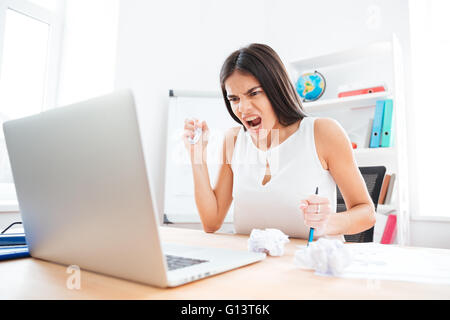 Arrabbiato imprenditrice seduta al tavolo e urlando in office Foto Stock
