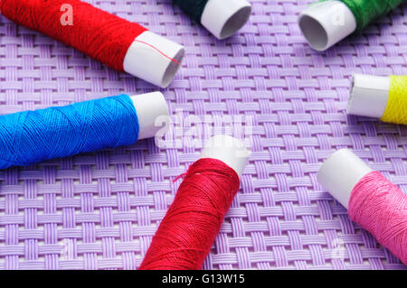 Bobine di filo per cucire di diversi colori su uno sfondo viola Foto Stock