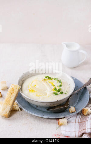 Terrina di asparagi bianchi minestra in crema con i germogli di piselli e toast, servito con una brocca del latte sulla tovaglia grigio Foto Stock