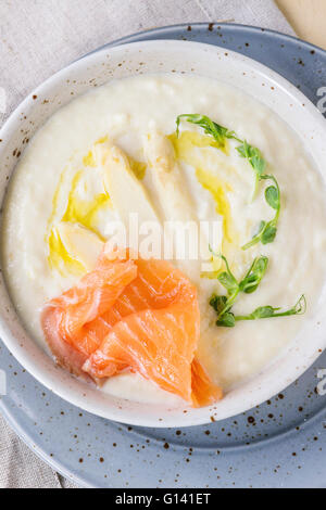 Terrina di asparagi bianchi minestra in crema con i cavoli bpeaean, salmone salato e toast sul tessile grigio igienico oltre bianco backgr in legno Foto Stock