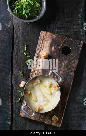 Vintage coppa in alluminio con asparagi bianchi minestra in crema con i germogli di piselli e toast, servita sul tagliere di legno su legno vecchio Foto Stock