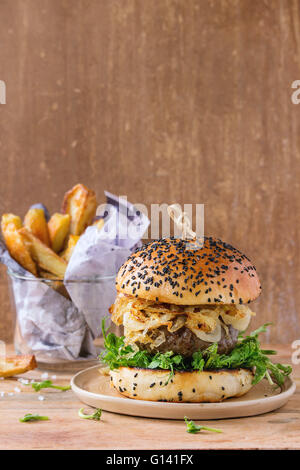 Hamburger fatti in casa a base di carne di manzo fritto di cipolla e germogli di piselli, servita su piastra in ceramica con patate fritte in legno backgr testurizzata Foto Stock