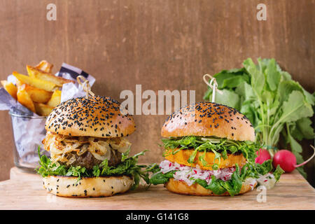 In casa tradizionale e veggie hamburger con carne di manzo, cipolla fritti, patata dolce, ravanello e germogli di piselli, servita su texture di legno Foto Stock