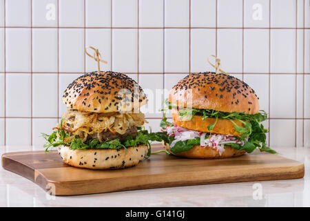 In casa tradizionale e veggie hamburger con carne di manzo, cipolla fritti, patata dolce, ravanello e germogli di piselli, servita su marmo bianco w Foto Stock