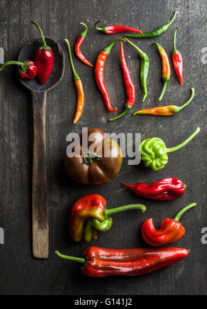 Il rosso e il verde di verdure e vecchio rustico cucchiaio in legno scuro di sfondo, vista dall'alto. Peperoni, chilis e pomodori kumato Foto Stock