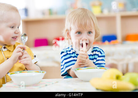 Kid mangiare in asilo nido e mostrando pollice in alto Foto Stock