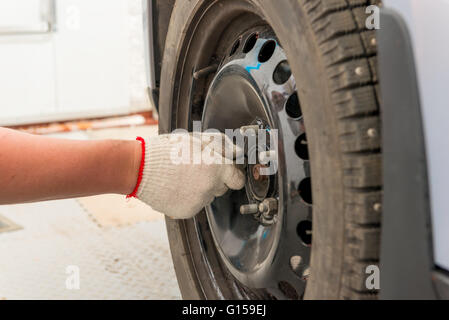 Mano d'uomo serrando le viti sulla ruota dopo l'installazione Foto Stock