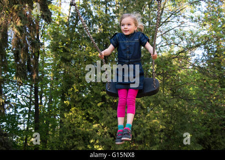 Bambino ragazza bionda divertirsi su altalena per esterno. Parco giochi estivo. Ragazza alta oscillante Foto Stock