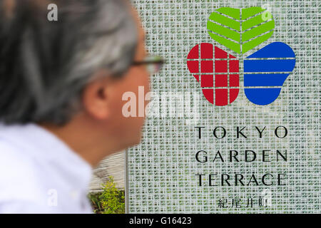 Tokyo, Giappone. Il 10 maggio, 2016. Un uomo cammina davanti a un cartello sul display esterno del Tokyo terrazza giardino Kioicho complesso in Chiyoda Ward su 10 Maggio 2016 a Tokyo, in Giappone. Il nuovo sviluppo da Seibu Holdings Inc. incorpora uffici, alberghi, alloggi di proprietà commerciali e sale conferenze, e comprende una torre principale di 38 piani e un lusso 23 piano complesso residenziale dietro di esso. Il progetto include anche la ristrutturazione e riapertura della Kitashirakawa palazzo che è stato costruito nel 1930 per l'ultimo principe della corona di Corea, Yi Onu che era anche un tenente generale nell'Imperial esercito giapponese. Foto Stock