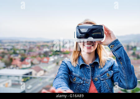 Donna che indossa la realtà virtuale gli occhiali di protezione in piedi su un balcone Foto Stock