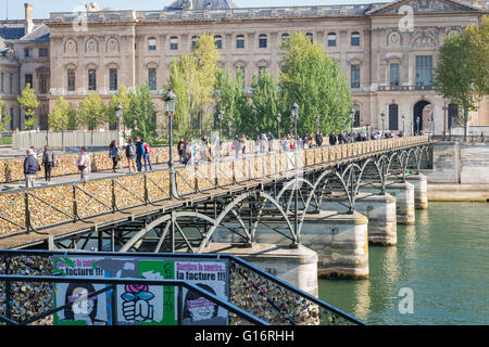 Pedoni attraversare il fiume Senna a Parigi sul Pont des Arts, ringhiere coperte di lucchetti. Museo del Louvre in background. Foto Stock