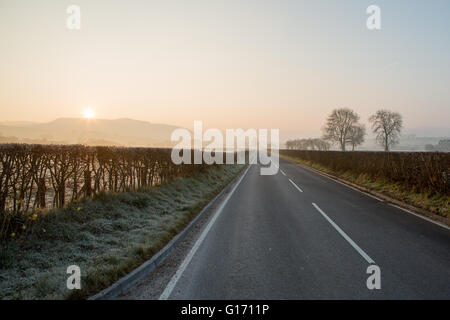 Misty sunrise con una lunga strada diritta Foto Stock